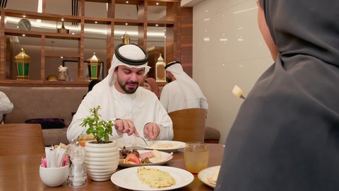 تشكيلة متنوعة من المأكولات على السفرة،  قضاء وقت ممتع ومسلي، الاستمتاع بتناول الأطباق الشهية، المطاعم و الكافيهات في الإمارات, زوجان عربيان خليجيان اماراتيان يرتديان الزي التقليدي يقومان بتناول الطعام، تقوية الروابط الزوجية والعائلية