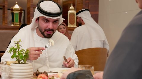 قضاء وقت ممتع ومسلي، الاستمتاع بتناول الأطباق الشهية، المطاعم و الكافيهات في الإمارات, زوجان عربيان خليجيان اماراتيان يرتديان الزي التقليدي يقومان بتناول الطعام، تشكيلة متنوعة من المأكولات على السفرة، تقوية الروابط الزوجية والعائلية