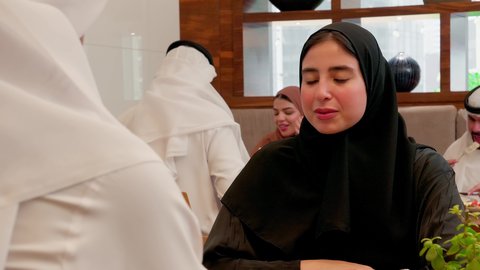 عائلة عربية خليجية اماراتية تجلس في المطعم،تصوير مقرب لامراة عربيه خليجيه اماراتية ترتدي الحجاب و العباءة تجلس برفقة زوجها تقوم بنقاشات وحوارات عائلية، ايماءات وجه ويدين تدل على السعادة، قضاء أوقات عائلية ممتعة، عطلة نهاية الاسبوع