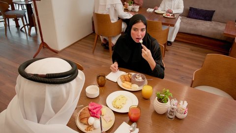 A table filled with a variety of delicious dishes, an upscale restaurant in the United Arab Emirates, love and affection between spouses, spending enjoyable time outside the home on the weekend, an Emirati Arab couple dining at the restaurant, the concept of a happy family.