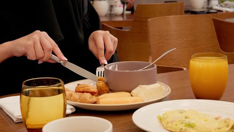 Enjoying breakfast, a close-up shot of a Gulf Arab Emirati woman using a knife and fork while eating in a restaurant, fresh orange juice on the table.