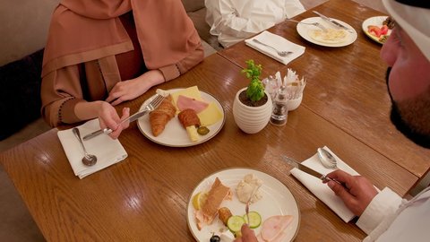 قضاء اوقات ممتعه، تصوير مقرب لزوجان عربيان خليجيان اماراتيان يرتدي الزي التقليدي يجلسان في مطعم, الاستمتاع بتناول الطعام, عطلة نهاية الاسبوع, تعارف وبناء علاقات اجتماعيه