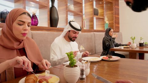 Enjoying lunch at the restaurant, spending the weekend outside, an Emirati Gulf Arab family wearing traditional attire sitting in the restaurant, serving the most delicious dishes and drinks, happy family atmosphere.