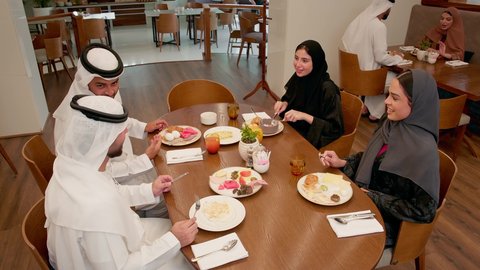 قضاء أوقات ممتعة في المطعم، تواصل أسري حيوي ونقاشات ودية، ايماءات السعادة والسرور، عطلة نهاية الاسبوع، عائله عربيه خليجيه اماراتية ترتدي الزي التقليدي يجلسون فى احد المطاعم يتناولون الافطار