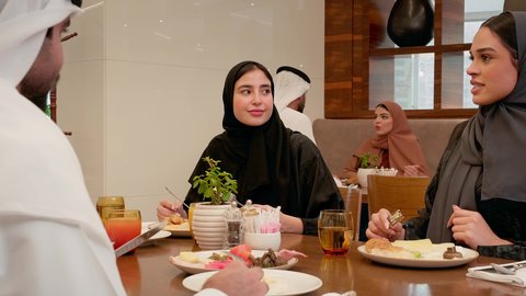 تبادل الأحاديث والآراء بين أفراد الأسرة، سفرة مليئة بالمأكولات والمشروبات، ايماءات السعادة والسرور، عطلة نهاية الاسبوع،الاستمتاع بتناول المشروبات، عائله عربيه خليجيه اماراتية ترتدي الزي التقليدي يجلسون فى احد المطاعم يتناولون الافطار