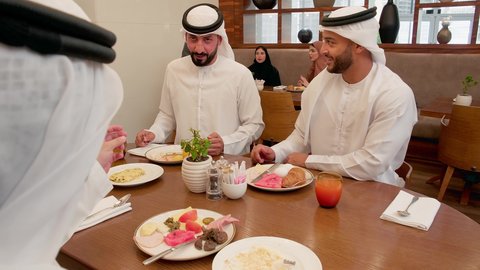نقاشات و حوارات عائليه على مائدة الطعام، عطلة نهاية الاسبوع، أجواء عائلية سعيدة، قضاء وقت ممتع، عائله عربيه خليجيه اماراتية ترتدي الكندورة و الغتره يجلسون فى احد المطاعم يتناولون الافطار، ايماءات السعادة والسرور