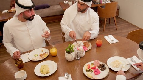 تدعيم أواصر المحبه والترابط الأسري، قضاء أوقات ممتعة، عائله عربيه خليجيه اماراتية ترتدي الكندورة و الغتره يجلسون فى احد المطاعم يتناولون الافطار ، سفرة مليئة بأطباق من المأكولات الشرقية المميزة