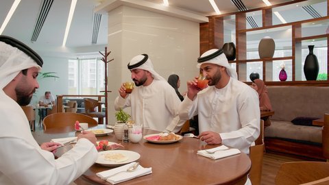 قضاء أوقات ممتعة، تدعيم أواصر المحبه والترابط الأسري، عائله عربيه خليجيه اماراتية ترتدي الكندورة و الغتره يجلسون فى احد المطاعم يتناولون الافطار ، الاستمتاع بتناول المشروبات ، سفرة مليئة بأطباق من المأكولات الشرقية المميزة