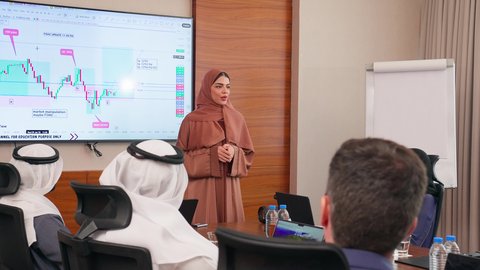موظفة اماراتية تعرض البيانات الاحصائية على الشاشة، ضمان فهم واضح وشامل للأعمال، تحقيق أهداف الشركة، استخدام الأجهزة التقنية الحديثة في المكاتب, الاتفاق على المشاريع التجارية، اجتماع عمل بين موظفين عرب خليجيين اماراتيين مع رجال أعمال أجانب في غرفة الاجتماعات