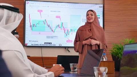 موظفة اماراتية تعرض البيانات الاحصائية على الشاشة، ضمان فهم واضح وشامل للأعمال، تحقيق أهداف الشركة، استخدام الأجهزة التقنية الحديثة في المكاتب, الاتفاق على المشاريع التجارية، اجتماع عمل بين موظفين عرب خليجيين اماراتيين مع رجال أعمال أجانب في غرفة الاجتماعات