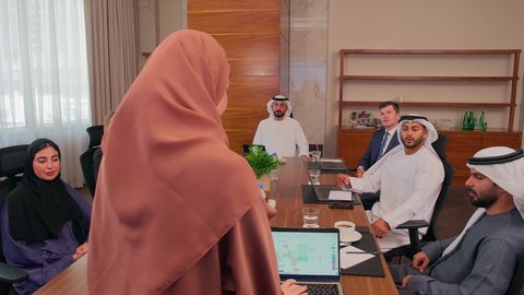 شرح وتوضيح العمليات والمشاريع والصفقات التجارية، التفاهم والتعاون بين الزملاء لتحقيق أهداف الشركة, نقاشات خاصة بالعمل, استخدام الحاسوب المحمول، اجتماع عمل مع موظفين عرب خليجيين اماراتيين مع رجال أعمال أجانب في غرفة الاجتماعات، ضمان فهم واضح وشامل للأعمال