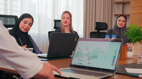 Dedication and professionalism in achievement, explaining operations and business deals, understanding and cooperation among colleagues to achieve the company's goals, work-related discussions, using a laptop, a business meeting with Emirati Gulf Arab employees and foreign businessmen in the meeting room, ensuring a clear understanding of the business.