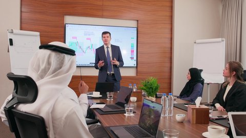ضمان فهم واضح وشامل للأعمال، تحقيق أهداف الشركة، استخدام الأجهزة التقنية الحديثة في المكاتب, موظف اجنبي يقوم بعرض البيانات الاحصائية على الشاشة، الاتفاق على المشاريع التجارية، اجتماع عمل بين موظفين عرب خليجيين اماراتيين مع رجال أعمال أجانب في غرفة الاجتماعات