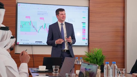 موظف اجنبي يقوم بعرض البيانات الاحصائية على الشاشة، ضمان فهم واضح وشامل للأعمال، تحقيق أهداف الشركة، استخدام الأجهزة التقنية الحديثة في المكاتب, الاتفاق على المشاريع التجارية، اجتماع عمل بين موظفين عرب خليجيين اماراتيين مع رجال أعمال أجانب في غرفة الاجتماعات