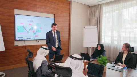 ضمان فهم واضح وشامل للأعمال، تحقيق أهداف الشركة، استخدام الأجهزة التقنية الحديثة في المكاتب, موظف اجنبي يقوم بعرض البيانات الاحصائية على الشاشة، الاتفاق على المشاريع التجارية، اجتماع عمل بين موظفين عرب خليجيين اماراتيين مع رجال أعمال أجانب في غرفة الاجتماعات