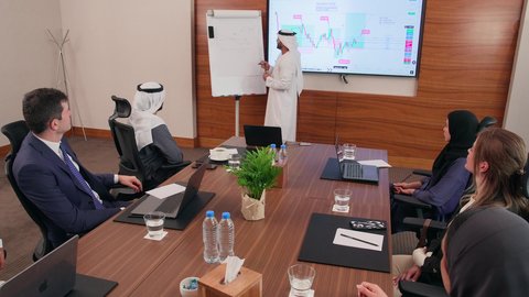 ضمان فهم واضح وشامل للأعمال، استخدام الأجهزة التقنية الحديثة في المكاتب, موظف اماراتي يقوم بعرض البيانات الاحصائية على الشاشة، الاتفاق على المشاريع التجارية، اجتماع عمل بين موظفين عرب خليجيين اماراتيين مع رجال أعمال أجانب في غرفة الاجتماعات، تحقيق أهداف الشركة