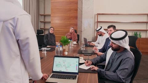 شرح وتوضيح العمليات والمشاريع والصفقات التجارية، التفاهم والتعاون بين الزملاء لتحقيق أهداف الشركة, نقاشات خاصة بالعمل, استخدام الحاسوب المحمول، اجتماع عمل مع موظفين عرب خليجيين اماراتيين مع رجال أعمال أجانب في غرفة الاجتماعات، ضمان فهم واضح وشامل للأعمال