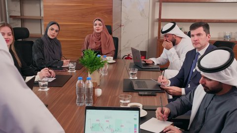 التفاهم والتعاون بين الزملاء لتحقيق أهداف الشركة, نقاشات خاصة بالعمل, استخدام الحاسوب المحمول، اجتماع عمل مع موظفين عرب خليجيين اماراتيين مع رجال أعمال أجانب في غرفة الاجتماعات، شرح وتوضيح العمليات والمشاريع التجارية، ضمان فهم واضح وشامل للأعمال