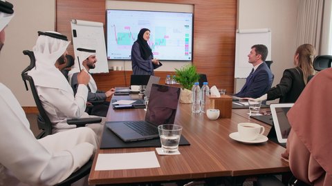 إنجاز المهام عبر جهاز الحاسوب، عرض البيانات الاحصائية على الشاشة، الاتفاق على المشاريع التجارية، اجتماع عمل بين موظفين عرب خليجيين اماراتيين مع رجال أعمال أجانب في غرفة الاجتماعات، بيئة العمل المريحة في الشركات الاماراتية, استخدام الأجهزة التقنية الحديثة في المكاتب