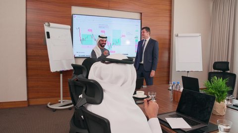 Discussion and exchange of ideas, presentation of plans and business projects, a business meeting between Emirati Gulf Arab employees and foreign businessmen in the meeting room, a comfortable work environment in Emirati companies, the use of modern technological devices in offices, completing work tasks via the computer.