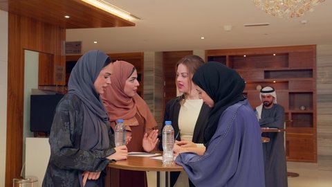 التعاون بين الموظفات العرب والاجانب، عقد صفقات عمل جديدة، الاتفاق على المشاريع التجارية، اجتماع فريق عمل عرب خليجيين اماراتيين مع وفد اجنبي في قاعة مؤتمرات فخمة، المناقشة وتبادل الافكار بين رجال الأعمال، معرض أعمال في الامارات العربية المتحدة مع المندوبين