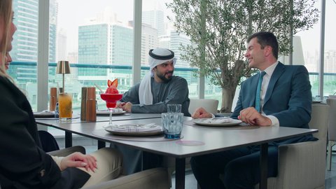 مناقشة وحوار عمل بين رجلين، المذاق الطيب للمأكولات والمشروبات، بناء علاقات اجتماعية ناجحة, اجتماع عمل في مكان خارج مقر الشركة, مشاركة الأوقات الممتعة, تصوير مقرب لمجموعة من الأصدقاء الاجانب والعرب خليجيين إماراتيين يجلسون على طاولة في إحدى المطاعم في الإمارات