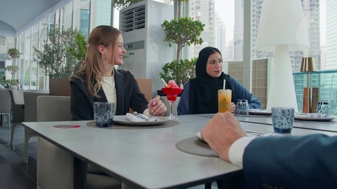 Friendships and acquaintances, delicious food and drinks, building successful social relationships, a business meeting outside the company headquarters, sharing fun times, a close-up of a group of foreign and Arab Gulf Emirati friends sitting at a table in a restaurant in the Emirates