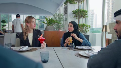 تبادل الأحاديث والاخبار, إيماءات السعادة والسرور، بناء علاقات اجتماعية ناجحة, اجتماع عمل في مكان خارج مقر الشركة, مشاركة الأوقات الممتعة, تصوير مقرب لمجموعة من الأصدقاء الاجانب والعرب خليجيين إماراتيين يجلسون على طاولة في إحدى المطاعم في الإمارات