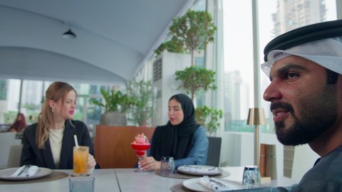 المذاق الطيب للمأكولات والمشروبات، إيماءات السعادة والسرور، بناء علاقات اجتماعية ناجحة, اجتماع عمل في مكان خارج مقر الشركة, مشاركة الأوقات الممتعة, تصوير مقرب لمجموعة من الأصدقاء الاجانب والعرب خليجيين إماراتيين يجلسون على طاولة في إحدى المطاعم في الإمارات