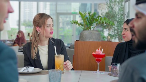 المناقشة وتبادل الأحاديث، إيماءات السعادة والسرور، بناء علاقات اجتماعية ناجحة, اجتماع عمل في مكان خارج مقر الشركة, مشاركة الأوقات الممتعة, تصوير مقرب لمجموعة من الأصدقاء الاجانب والعرب خليجيين إماراتيين يجلسون على طاولة في إحدى المطاعم في الإمارات