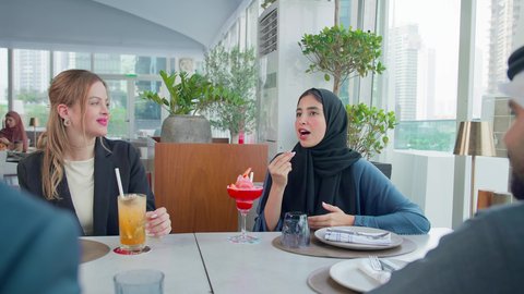 إيماءات السعادة والسرور، بناء علاقات اجتماعية ناجحة, اجتماع عمل في مكان خارج مقر الشركة, شرب المشروبات الباردة, مشاركة الأوقات الممتعة, المناقشة وتبادل الأحاديث، مجموعة من الأصدقاء الاجانب والعرب خليجيين إماراتيين يجلسون على طاولة في إحدى المطاعم في الإمارات