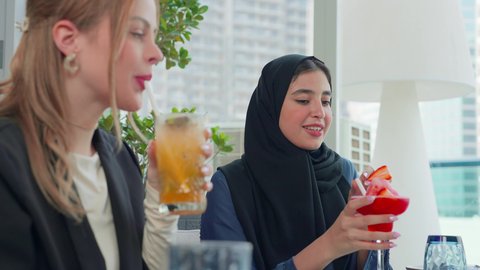 بناء علاقات اجتماعية ناجحة، العمل عن بعد في احدى مطاعم الامارات العربية المتحدة, اجتماع عمل في مكان خارج مقر الشركة,   تناول المشروبات الباردة في الاستراحة، تصوير مقرب لسيدتان اعمال احداهم من الاجانب والاخرى عربية  خليجية اماراتية يجلسون على طاولة
