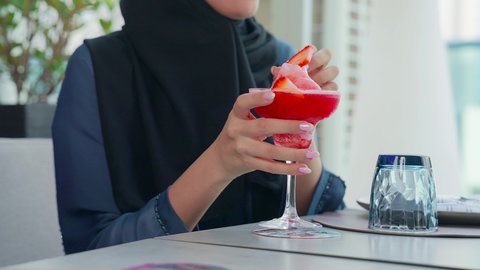 متعة المشروبات الباردة، العمل عن بعد في احدى مطاعم الامارات العربية المتحدة, اجتماع عمل في مكان خارج مقر الشركة,   تناول المشروبات الباردة في الاستراحة، تصوير مقرب لسيدة اعمال عربية  خليجية ترتدي الحجاب والعباءة اماراتية تجلس على طاولة