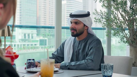 الاستمتاع بأجواء هادئه خارج مقر الشركة، العمل عن بعد في احدى مطاعم الامارات العربية المتحدة, اجتماع عمل في مكان خارج مقر الشركة,   تناول وجبة الغداء في الاستراحة، تصوير مقرب لرجل اعمال عربي خليجي اماراتي يجلس على مائدة مليئة بالأطعمة، بناء علاقات اجتماعية ناجحة