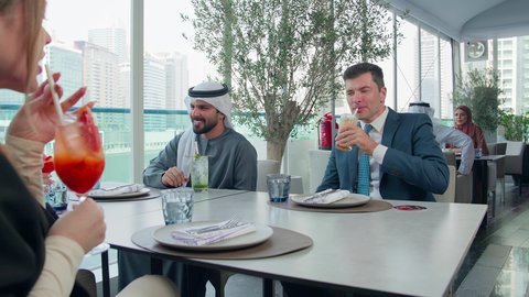 اجتماع عمل في مكان خارج مقر الشركة,  شرب المشروبات الباردة, مشاركة الأوقات الممتعة, المناقشة وتبادل الأحاديث، بناء علاقات اجتماعية ناجحة, مجموعة من الأصدقاء الاجانب والعرب خليجيين إماراتيين يجلسون على طاولة في إحدى المطاعم في الإمارات