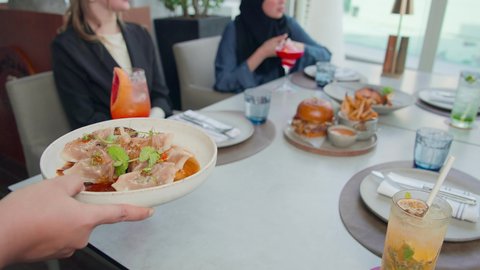 سService in an Emirati restaurant, a waiter serving Western dishes, a business meeting in a place outside the company headquarters, spending a pleasant time with friends, a session of fun and getting to know each other, a group of Emirati Gulf Arab friends sitting at a table in a restaurant in the Emirates, eating their favorite meals