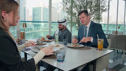 الاستمتاع بتناول الغداء في المطعم, مشاركة الأصدقاء الأوقات الممتعة, بناء علاقات اجتماعية ناجحة, تبادل الأحاديث والاخبار, مجموعة من الأصدقاء الاجانب والعرب خليجيين إماراتيين يجلسون على المائدة في إحدى المطاعم في الإمارات بإيماءات السعادة والسرور