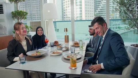 التقاط صورة باستخدام الهاتف المحمول، الاستمتاع بتناول الغداء في المطعم, مشاركة الأصدقاء الأوقات الممتعة, بناء علاقات اجتماعية ناجحة, تبادل الأحاديث والاخبار, مجموعة من الأصدقاء الاجانب والعرب خليجيين إماراتيين يجلسون على المائدة في إحدى المطاعم في الإمارات