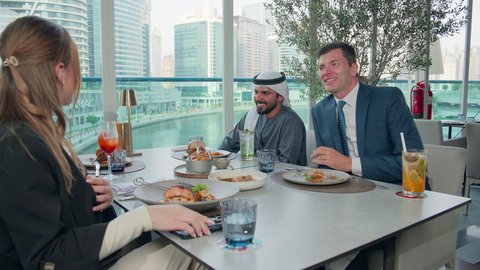 صورة لتوثيق لحظات مهمة, اجتماع عمل في مكان خارج مقر الشركة, الاستمتاع بتناول الغداء في المطعم, مشاركة الأصدقاء الأوقات الممتعة, بناء علاقات اجتماعية ناجحة, مجموعة من الأصدقاء الاجانب والعرب خليجيين إماراتيين يجلسون على المائدة في إحدى المطاعم في الإمارات