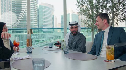 مشاركة الأوقات الممتعة, الاستمتاع بتناول المشروبات الباردة, الدفع باستخدام الفيزا فاتورة الغداء, اجتماع عمل في مكان خارج مقر الشركة, بناء علاقات اجتماعية ناجحة, مجموعة من الأصدقاء الاجانب والعرب خليجيين إماراتيين يجلسون على طاولة في إحدى المطاعم في الإمارات
