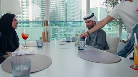 الدفع باستخدام الفيزا فاتورة الغداء, اجتماع عمل في مكان خارج مقر الشركة, الاستمتاع بتناول المشروبات الباردة, مشاركة الأوقات الممتعة, بناء علاقات اجتماعية ناجحة, مجموعة من الأصدقاء الاجانب والعرب خليجيين إماراتيين يجلسون على طاولة في إحدى المطاعم في الإمارات