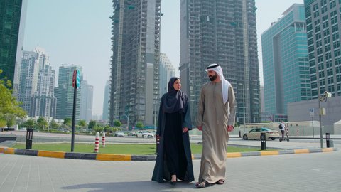 Pride and admiration for architectural progress, walking around and breathing fresh air outside, watching the urban development in the city, identifying a specific location, urban growth in the Emirates, an Arab Gulf Emirati couple wearing Emirati dress pointing at something