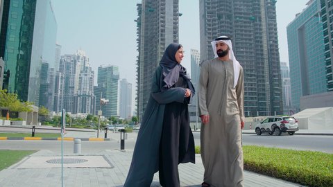 التجول واستنشاق الهواء النقي في الخارج,  مشاهدة التطور العمراني في المدينة، تحديد موقع معين ،الفخر والاعتزاز بالتقدم المعماري ، النمو العمراني في الامارات ،زوجان عربيان خليجيان اماراتيان يرتديان الزي الاماراتي يشيران الي شئ ما