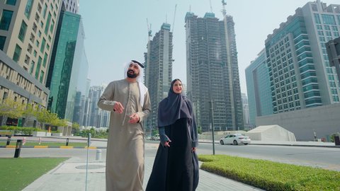 تحديد موقع معين ، مشاهدة التطور العمراني في المدينة، التجول واستنشاق الهواء النقي في الخارج, الفخر والاعتزاز بالتقدم المعماري ، النمو العمراني في الامارات ،زوجان عربيان خليجيان اماراتيان يرتديان الزي الاماراتي يشيران الي شئ ما