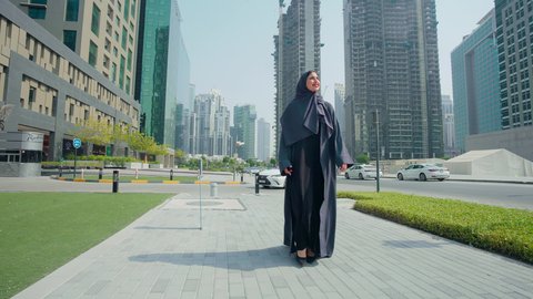 Outdoor walk, watching the urban development in the city, urban growth in the Emirates, pride and admiration for the architectural progress, an Arab Gulf Emirati woman wearing an abaya and hijab walking outside