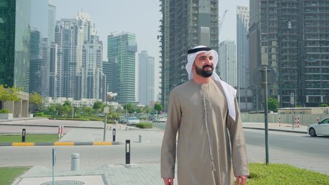 الفخر والاعتزاز بالتقدم المعماري ، استنشاق الهواء النقي , مشاهدة التطور العمراني في المدينة، النمو العمراني في الامارات ،رجل عربي خليجي اماراتي  يرتدي الكندورة والغتره يتجول فى الخارج