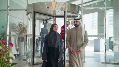 الاستمتاع بالشراء والتبضع، إقتناء المستلزمات من المولات، متعة التسوق مع العائلة، الإستفادة من العروض والحسومات والتخفيضات الموسمية، زوجان عربيان خليجيان اماراتيان يتجولان في المول ، إيماءات السعادة والسرور