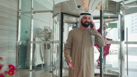 استخدام الهاتف المحمول ، اجراء مكالمه هاتفيه ، الاستمتاع بالشراء والتبضع، إقتناء المستلزمات من المولات، رجل عربي خليجي اماراتي يرتدي الكندورة والغترة يتجول فى المول