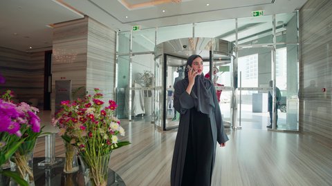 اجراء مكالمه هاتفيه ، استخدام الهاتف المحمول ، الاستمتاع بالشراء والتبضع، إقتناء المستلزمات من المولات، ، امراه عربيه خليجيه اماراتيه ترتدي العباءه والحجاب تتجول فى المول