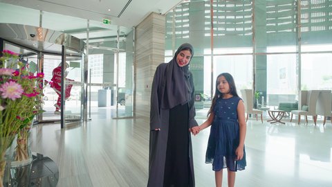 امراه عربية خليجية اماراتيه ترتدي العباءه والحجاب تضع وردة على شعر ابنتها بتعابير الحب, مفهوم الأسرة السعيدة ، قضاء أوقات عائلية ممتعة، مشاعر الأمومة  والاهتمام، إقتناء المستلزمات من المولات،الإستفادة من العروض والحسومات والتخفيضات الموسمية